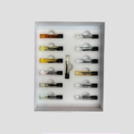 Tray of small sample vials arranged in a white foam insert inside a shallow box, likely perfume or extract samples.
